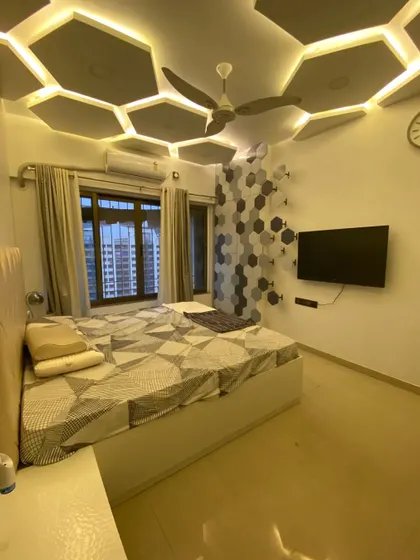 A master bedroom designed with a unique hexagonal theme. The geometric pattern on the TV wall is complemented by a stunning false ceiling with backlit hexagonal panels.
