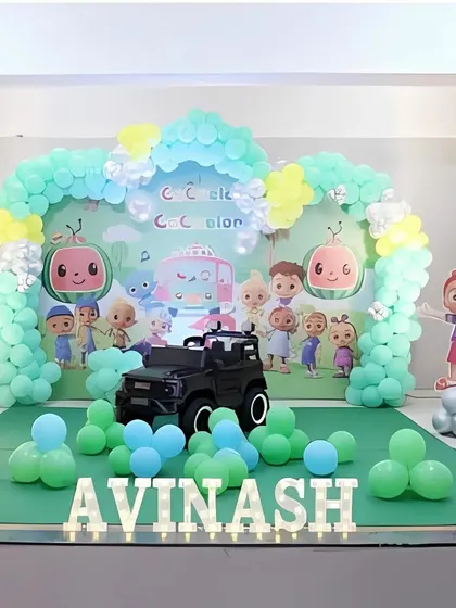 A wide shot of the Cocomelon birthday stage, showing the full arrangement including the character standee and balloon clusters on the floor.