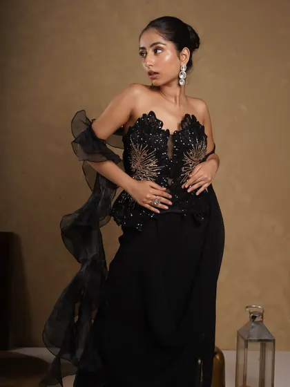 A modern take on ethnic evening wear. This shot showcases a structured peplum top with intricate black and gold embroidery, paired with a flowing draped skirt.