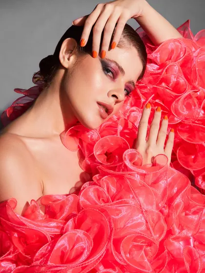 A high-fashion look where the makeup is paired with a dramatic, ruffled outfit and bright orange nails.
