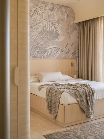 The guest bedroom in Soft Serve evokes the calming ambiance of a bed and breakfast, with muted neutral tones, curved wooden furniture, and a beautiful botanical mural.