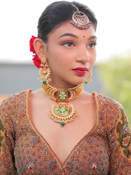 A model showcasing a traditional gold-toned choker with green enamel work and a central pendant. This style of jewellery is timeless and adds an element of heritage.