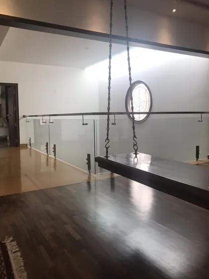 Light from a high window reflects off the polished wooden floor of a landing, which features a traditional swing and a modern glass balustrade.