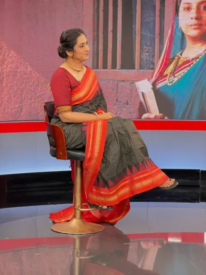 A full view of the on-set look. The elegant saree draping and simple hairstyle complete this professional and polished appearance for her television feature.