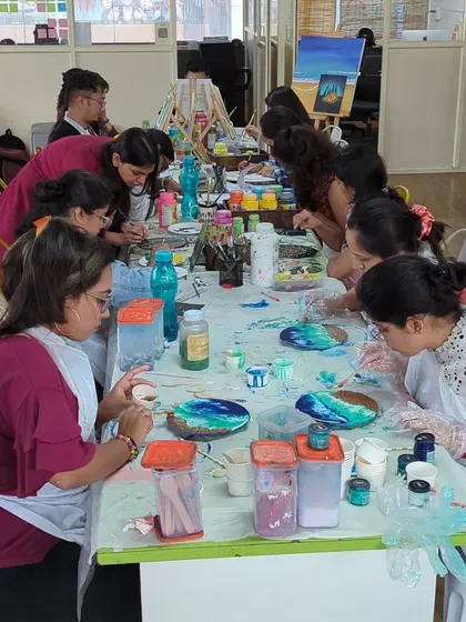 A group of participants fully engaged in a resin art workshop, carefully mixing colors and pouring them onto their projects. It's a focused, fun, and wonderfully messy process!