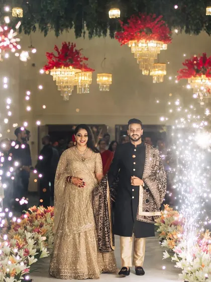 A stunning reception entrance. The couple walks down an aisle illuminated by sparklers, with grand floral chandeliers hanging overhead, creating an atmosphere of pure celebration.