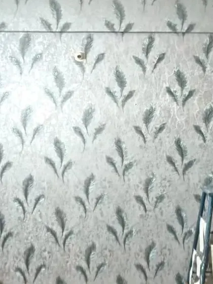 A close-up of a textured wallpaper with a silver feather pattern, showing the metallic sheen that catches the light.