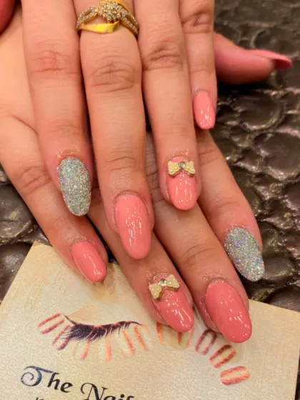 A sweet and charming set of peach-colored almond nails. The design includes silver glitter accent nails and cute 3D bows with a pearl center.