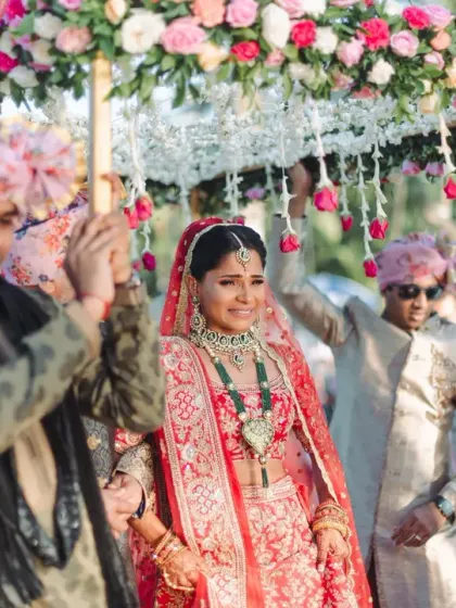 The bride's grand entrance under a beautiful floral canopy held by her brothers. Her happy, confident smile shows she is ready to step into her new life.