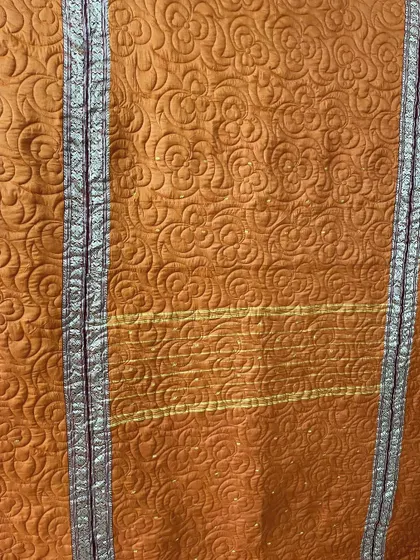 Close-up of an orange saree quilt, highlighting the texture of the longarm quilting and the preserved silver border.