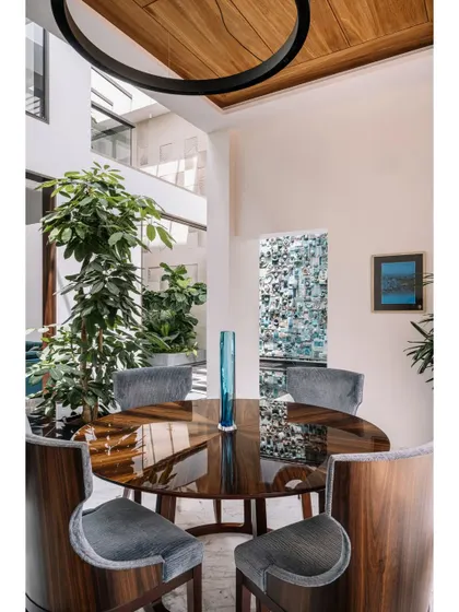 The dining area is nestled within the open-plan layout, with a direct view of the courtyard's greenery and the stunning turquoise mural. The use of a round table encourages conversation, making it a warm and intimate space for meals.