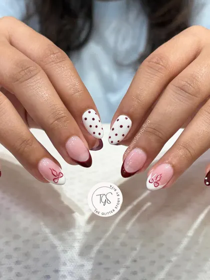 A playful and chic nail set combining different designs. It features a deep red French tip, red and white polka dots, and delicate bow art.