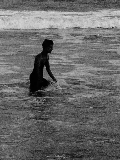 A boy wades into the ocean surf. This simple black and white image captures a quiet moment of interaction between a person and the vastness of the sea.