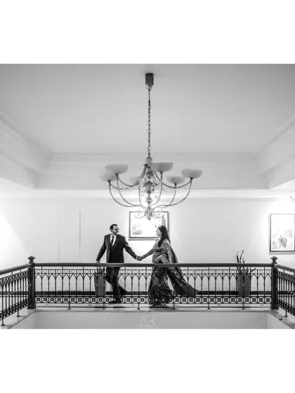 A wide, architectural shot of the couple on a balcony. Converting this to black and white highlights the elegant lines of the railing and chandelier, giving it a grand, classic feel.