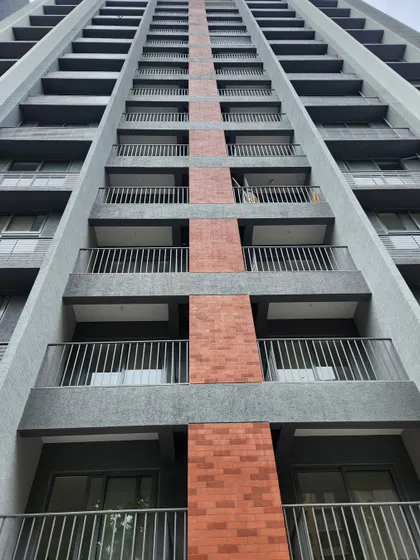 A close up of the facade at Adani Amogha, Ahmedabad. The vertical band of brick-colored tiles contrasts with the grey concrete finish, breaking the scale of the building and adding a touch of warmth to the exterior.
