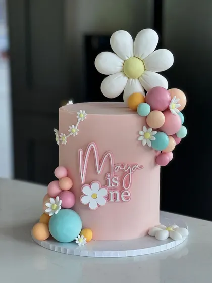 A groovy and cute daisy-themed cake for Maya's first birthday. The pastel colors and fun balloon clusters give it a retro, cheerful vibe.