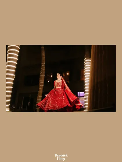 A wide shot of the bride in her stunning red Falguni Shane Peacock lehenga, standing between two illuminated palm trees at night.