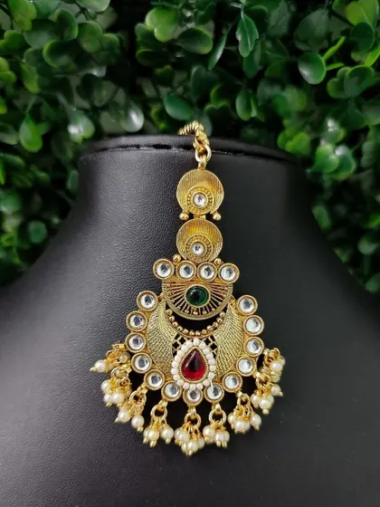A traditional temple-style maang tikka with an antique gold finish. The red and green stones give it a classic, timeless appeal.