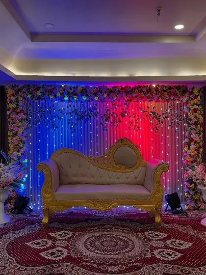 A simple yet impactful stage design with a fairy light backdrop, a classic diwan, and dramatic red and blue uplighting for a vibrant look.