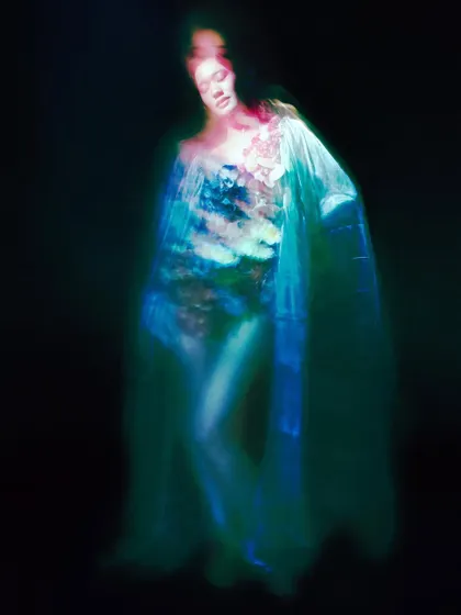 A dark, moody shot where the model appears as a spectral figure illuminated by faint blue and green light. The image is haunting and beautiful, capturing the essence of a tragic spirit.