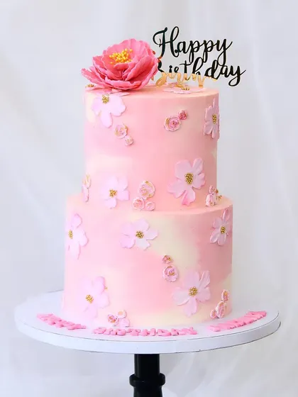 A charming two-tiered cake featuring delicate pink flowers against a soft pink and white buttercream base. This design is perfect for birthdays, anniversaries, or any event calling for a touch of floral grace.