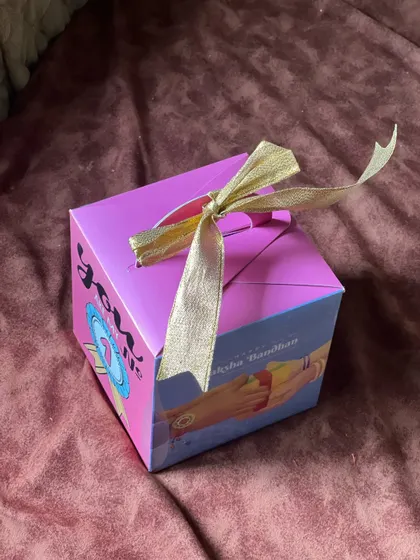 A compact and colorful Rakhi gift box, perfect for sending a token of love. The box itself is decorated with traditional Raksha Bandhan imagery.