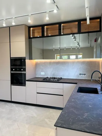 This kitchen design combines beige handleless cabinets with a dark countertop and mirrored backsplash. The mirror is a great way to make a smaller kitchen feel more spacious and bright.