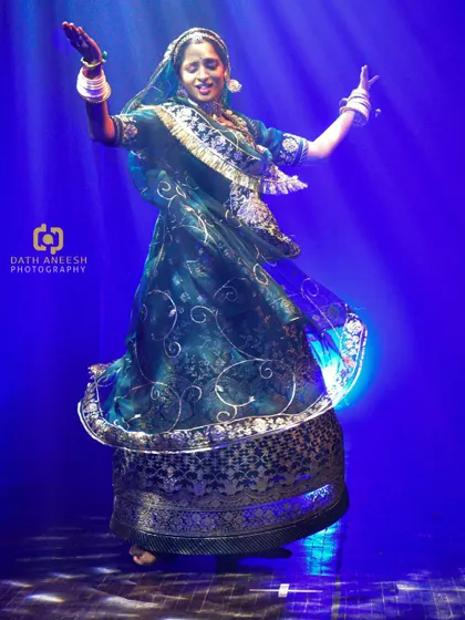 A full-body shot of my Ghoomar performance, showing the grace and flow of the traditional poshak as I twirl under the blue stage lights.