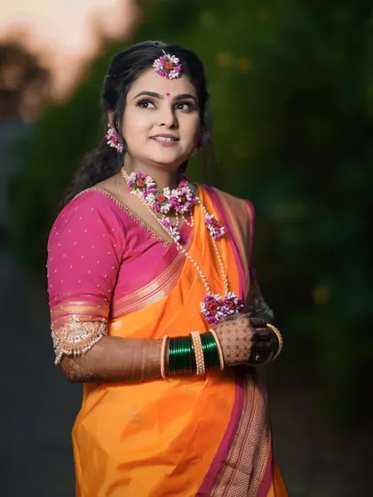 A beautiful portrait of a bride ready for her Haldi ceremony. She is adorned with floral jewelry that perfectly complements her orange and pink saree.
