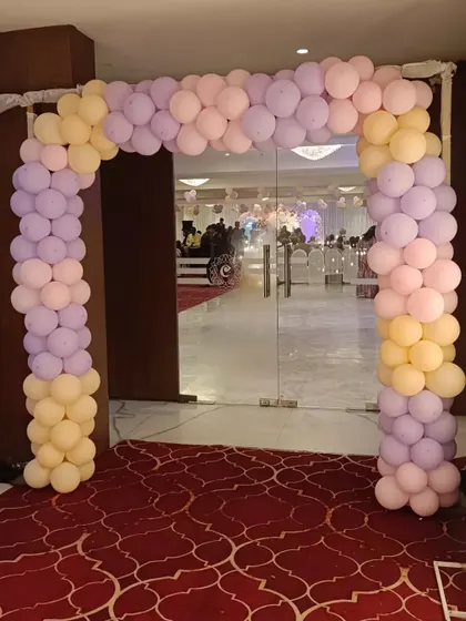 A classic pastel balloon arch in pink, purple, and yellow. This decoration is placed at the glass entrance of a hall, giving guests a hint of the party's color scheme before they even step inside.