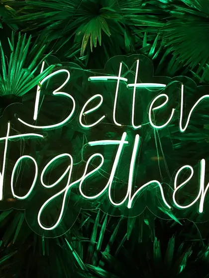A trendy 'Better Together' neon sign against a green foliage backdrop, a popular decor element we love to photograph.