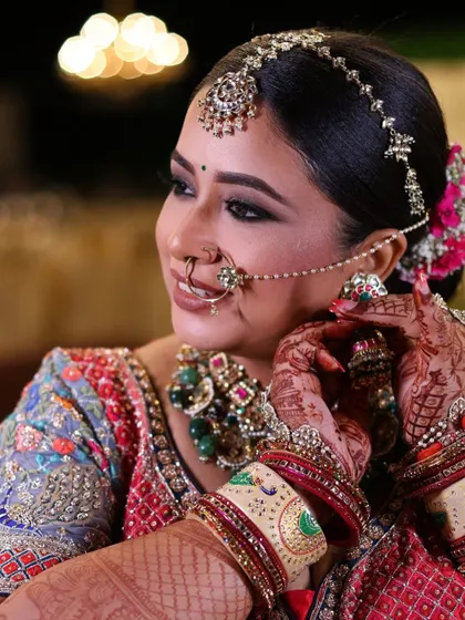 A candid shot of the bride smiling, her hands framing her face, showing off her intricate henna and bridal bangles.