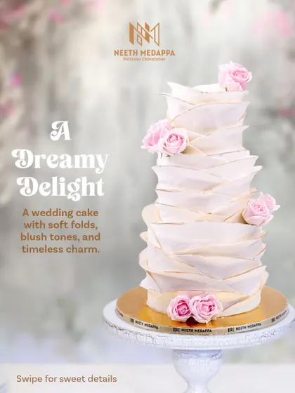 A dreamy, multi-tiered wedding cake with soft, handcrafted folds and delicate blush-pink roses. The design evokes a sense of gentle movement and timeless charm, perfect for a romantic celebration.