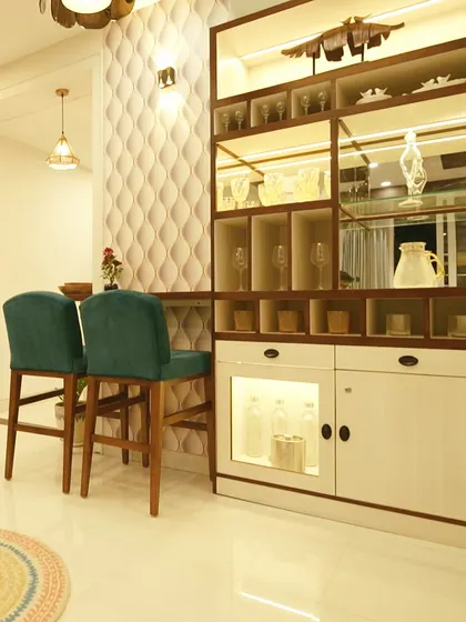 A custom-designed bar and crockery unit with integrated lighting. The textured 3D paneling on the wall and stylish bar stools create a chic entertainment corner.