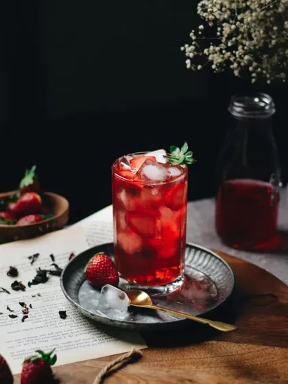 A moody and dramatic shot of a strawberry iced tea. The dark background makes the vibrant red of the drink pop, creating a sophisticated and refreshing visual perfect for a summer menu.