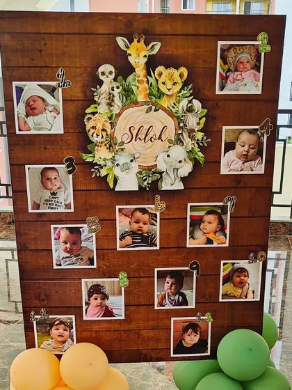 A custom photo milestone board for Shlok's first birthday. This wooden board displays monthly photos from his first year, surrounded by adorable jungle animal illustrations, making for a cherished keepsake.