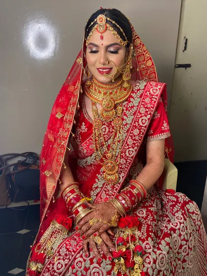 A full seated portrait showing the grandeur of the red lehenga and the perfectly coordinated makeup.