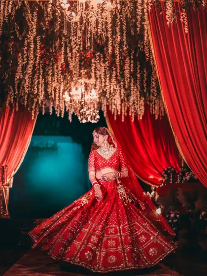 A bride twirls in her red lehenga under a canopy of flowers and red curtains, creating a vibrant and dynamic shot.
