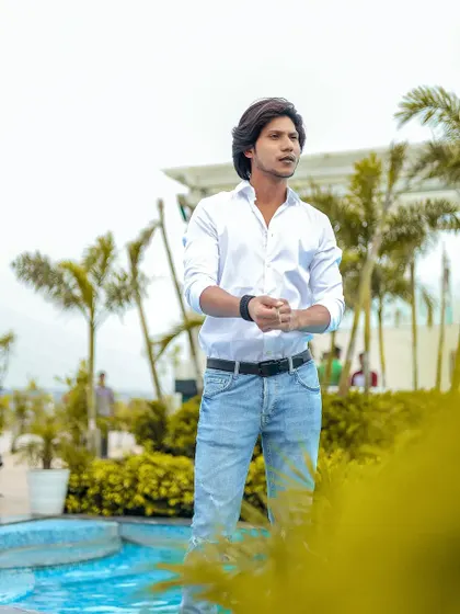 A casual men's portrait at a poolside location with lush greenery.