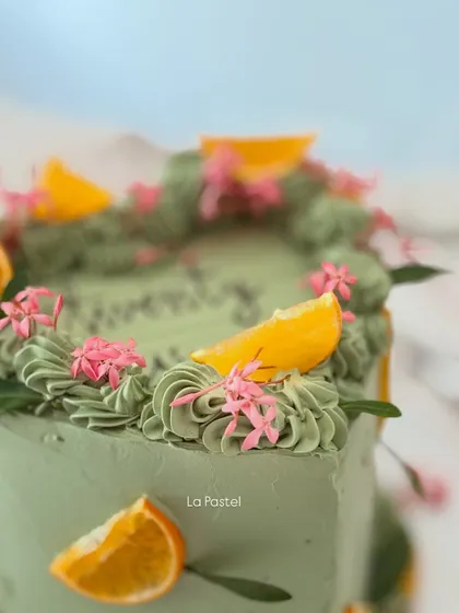 A close-up shot of the vibrant orange slices and pink flowers on the green heart cake.