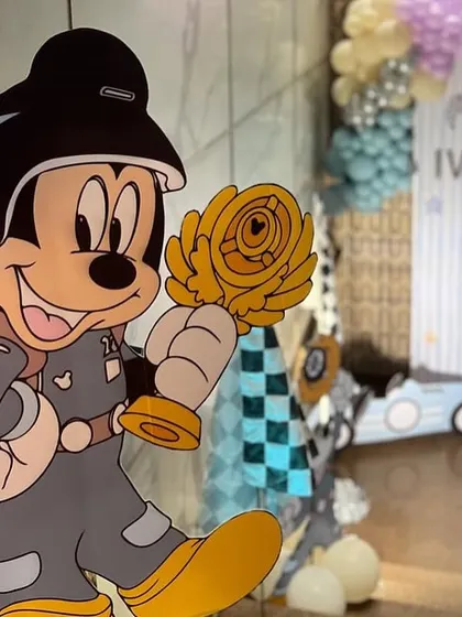 A detailed cutout of Mickey Mouse in a racing uniform, holding a trophy, showcasing the high-quality props we use.