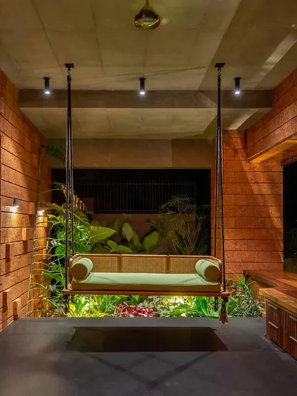 A beautiful swing on a covered patio, with a backdrop of lush, illuminated plants. This setup creates a perfect relaxation spot, combining the comfort of an indoor room with the beauty of an outdoor garden.