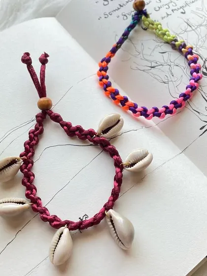 A pair of my beach-inspired anklets. One design features a deep red braided band adorned with natural cowrie shells for a classic beachy look, while the other is a vibrant, multi-colored braided anklet. Both are adjustable for a comfortable fit.