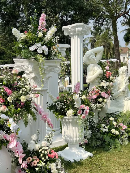 A collection of Roman-inspired statues and pedestals, each adorned with unique floral arrangements, creating artistic photo opportunities for guests.