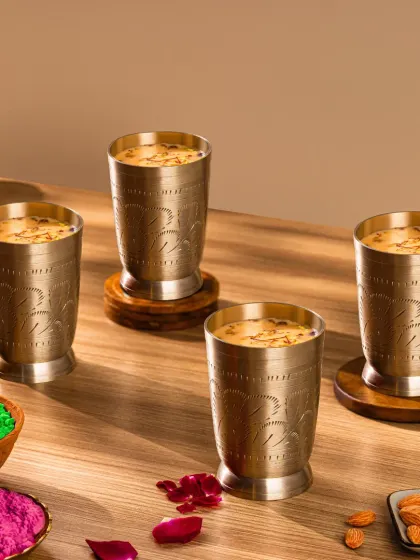 This shot focuses on the prepared Thandai in traditional glasses, surrounded by Holi colors and ingredients. The warm, directional lighting creates an inviting and celebratory atmosphere.