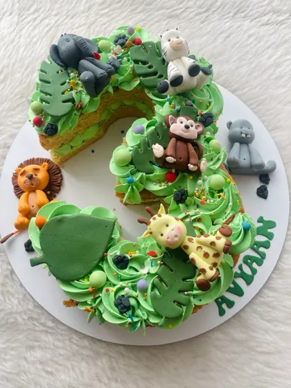 A number three cake with a jungle twist. The cake itself is shaped and decorated with green frosting and edible leaves, with lots of cute jungle animals joining the party.