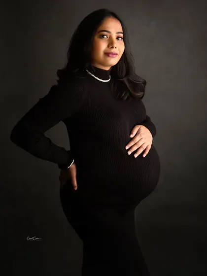 A confident and stylish portrait. This mom-to-be looks directly at the camera, her hand on her hip, radiating power in a simple black dress.