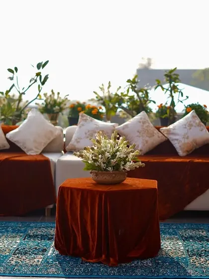 An inviting outdoor seating arrangement with plush white cushions on a rust-colored velvet-draped sofa. The look is completed with a Persian-style rug and a floral centerpiece.