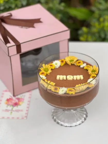 A hug in a bowl for Mother's Day. This is our handcrafted dark chocolate mousse, delicately decorated with fresh yellow and white blooms and the word "mom" in white chocolate. It comes packaged in our pink window box.