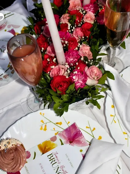 An overhead shot of a beautiful birthday brunch tablescape. The floral centerpiece, custom menus, and delicious cupcakes create a chic and celebratory setting.